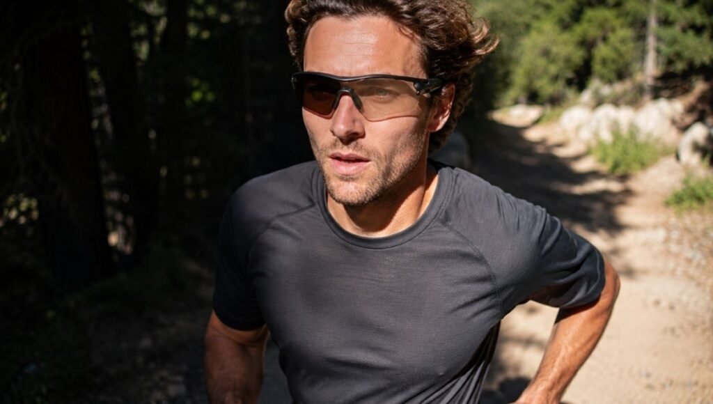 Trail runner moving from shaded forest into bright sunlight wearing photochromic running sunglasses